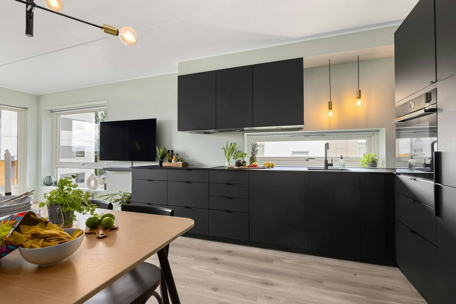 Modern minimalist kitchen with matte black cabinets, built-in oven, hanging lights, and sleek black faucet – Contourly home interior inspiration.